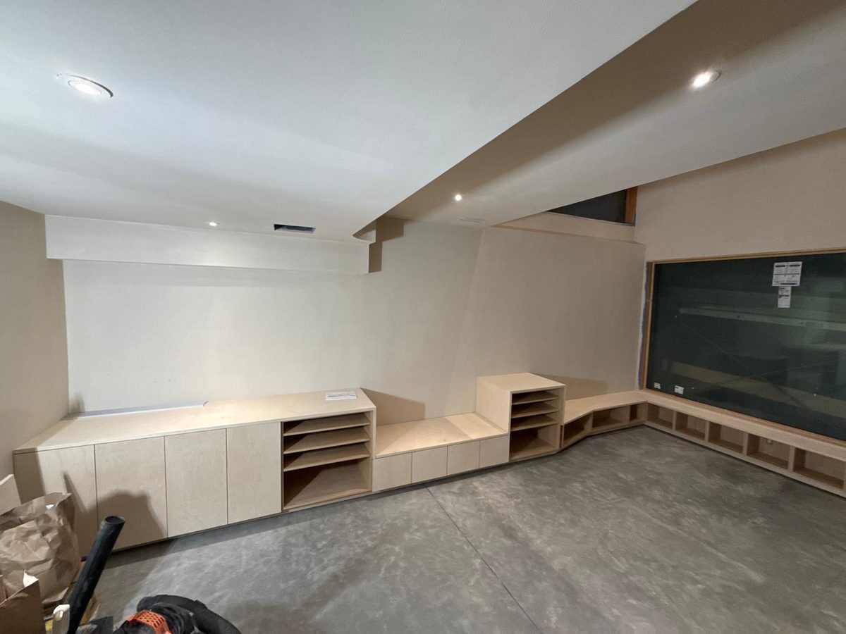 Basement built-ins: tall storage, open shelves, a bench seat and window-seat cubbies on polished concrete