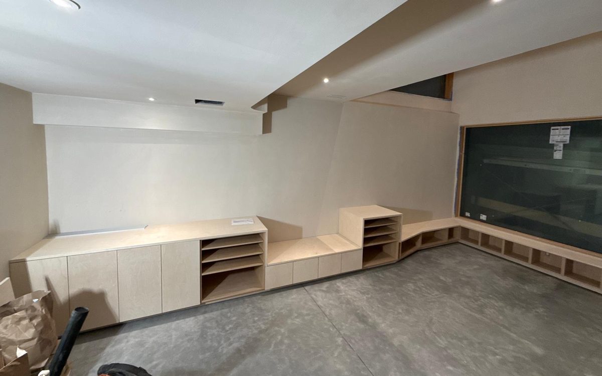 Basement built-ins: tall storage, open shelves, a bench seat and window-seat cubbies on polished concrete