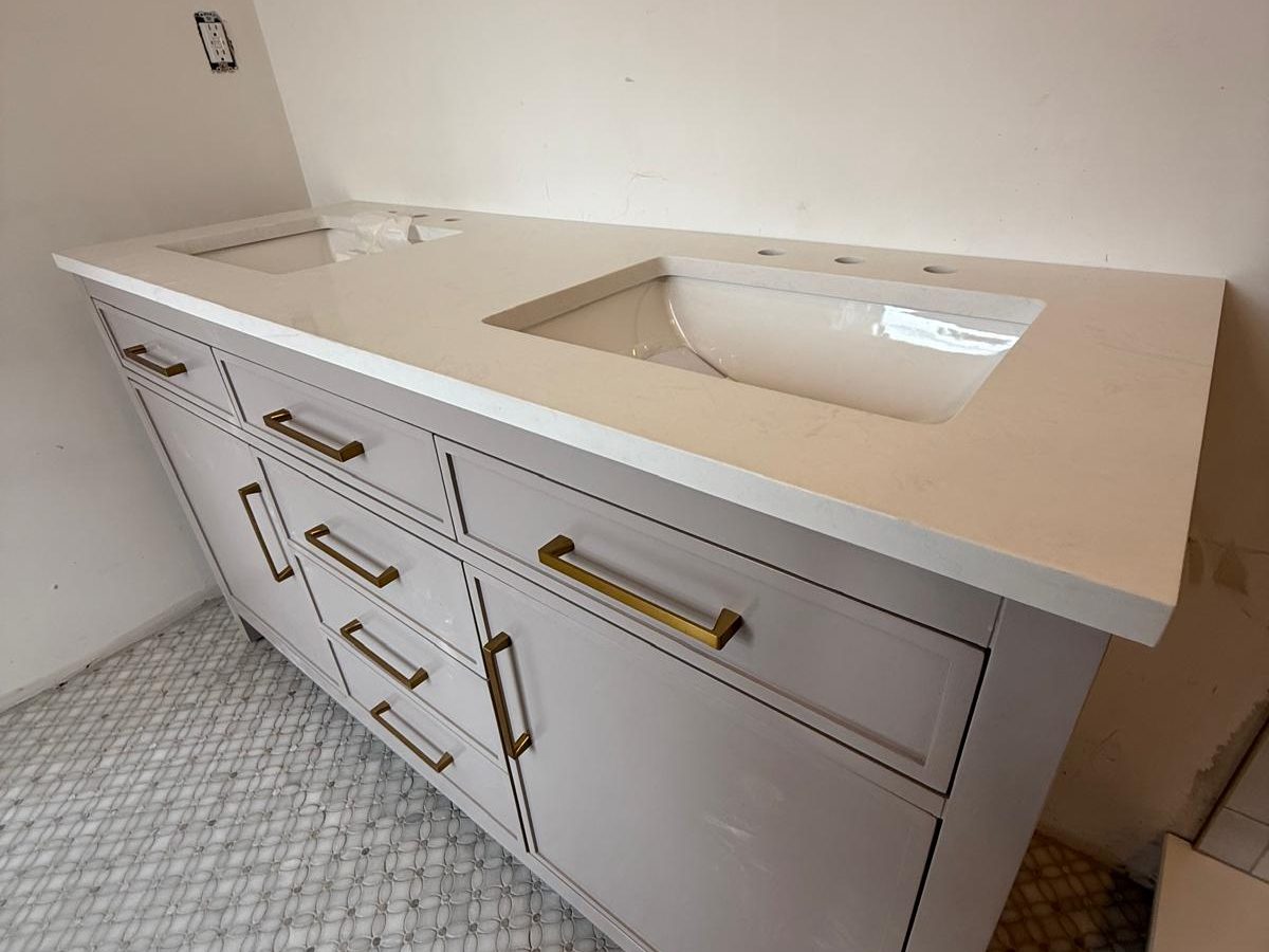 Gray shaker vanity with a quartz top and brushed brass pulls on a marble mosaic floor