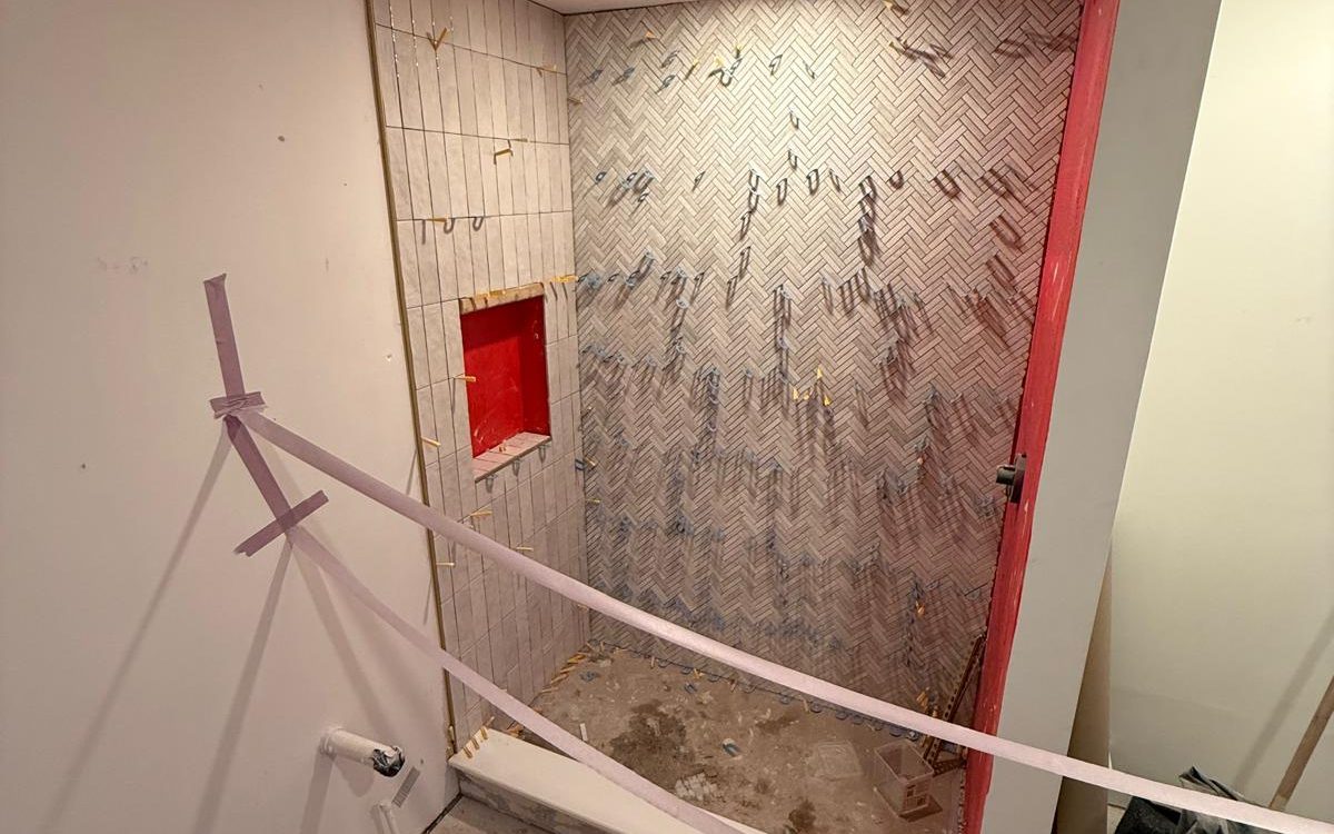 Herringbone and vertical wall tile held by leveling clips, with the niche still showing red waterproofing
