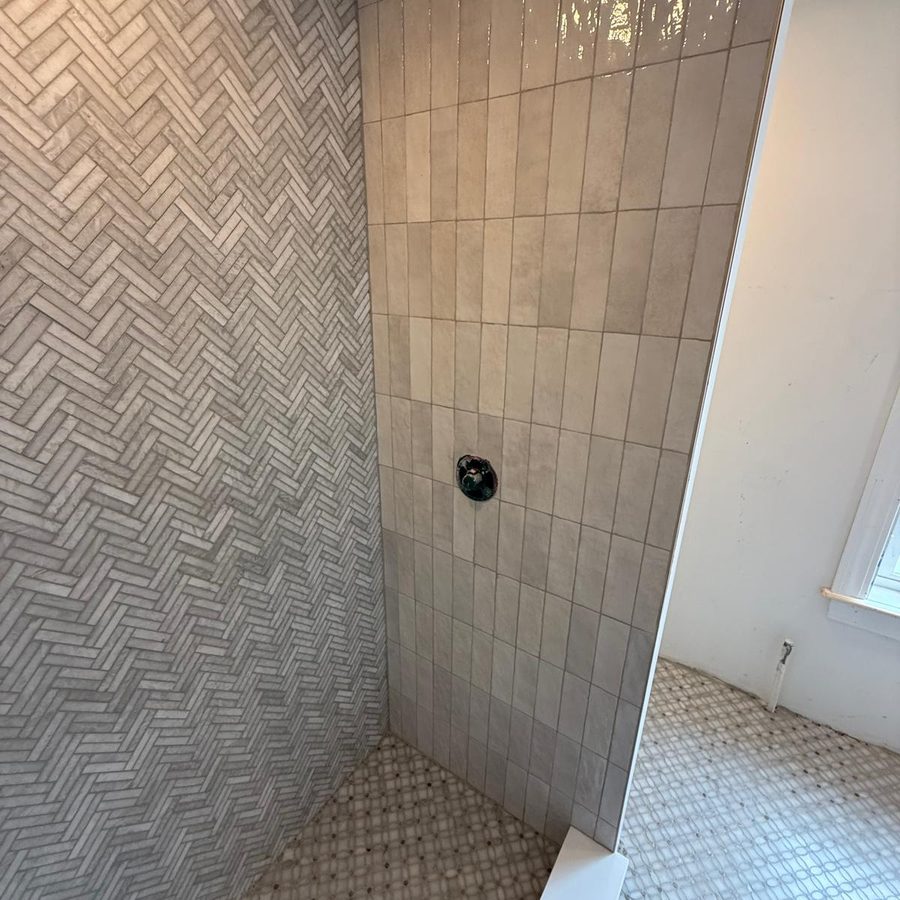 Shower corner where the herringbone wall meets vertical glazed tile above a mosaic floor