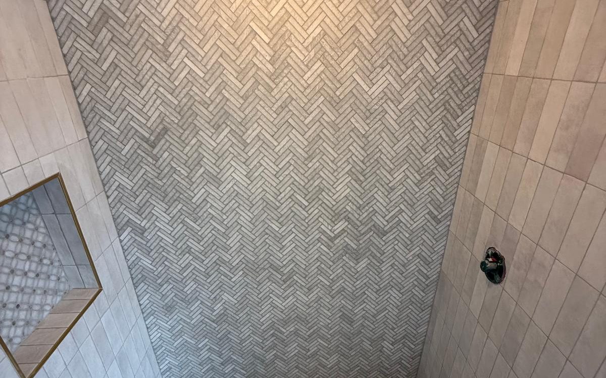 View into the herringbone shower with a centered drain and brass-trimmed niche