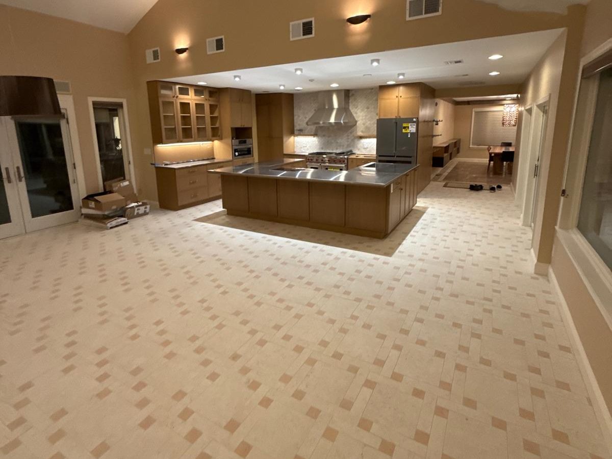 After: Finished kitchen and family room with woven tile floor, wood cabinets and a stainless-topped island