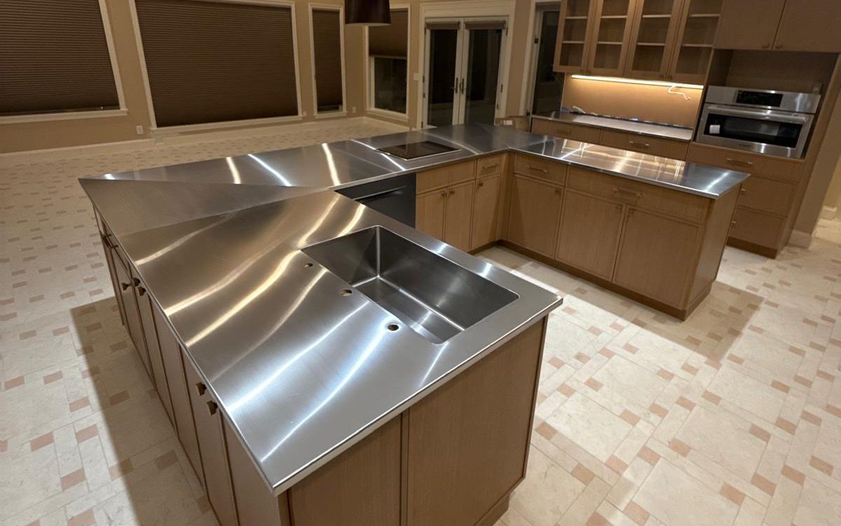 L-shaped island with a stainless steel countertop and integrated sink on the new tile floor