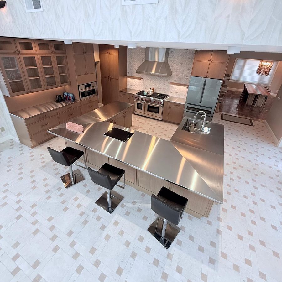 Kitchen seen from the loft: stainless island with bar stools, glass-front cabinets and woven tile floor