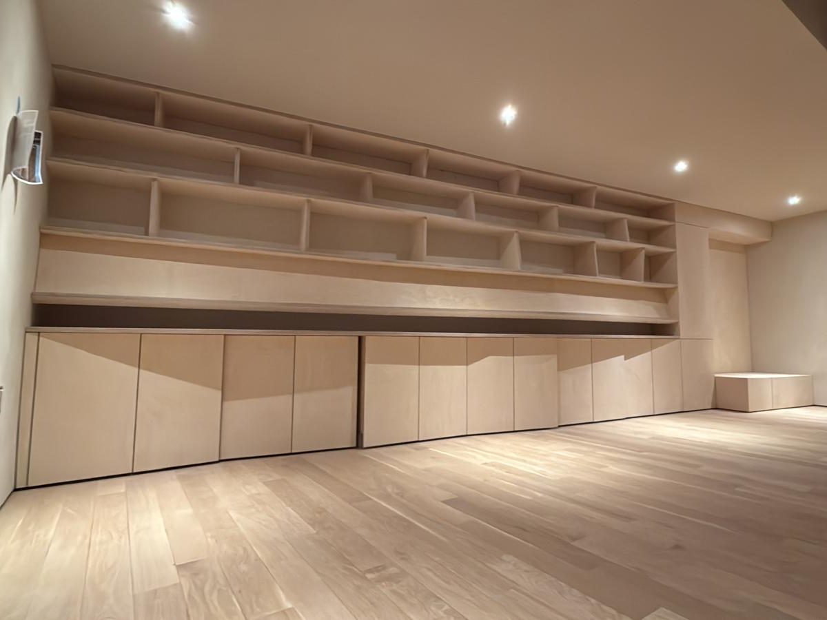 Wall of built-in birch shelves with angled dividers above a row of flush cabinet doors
