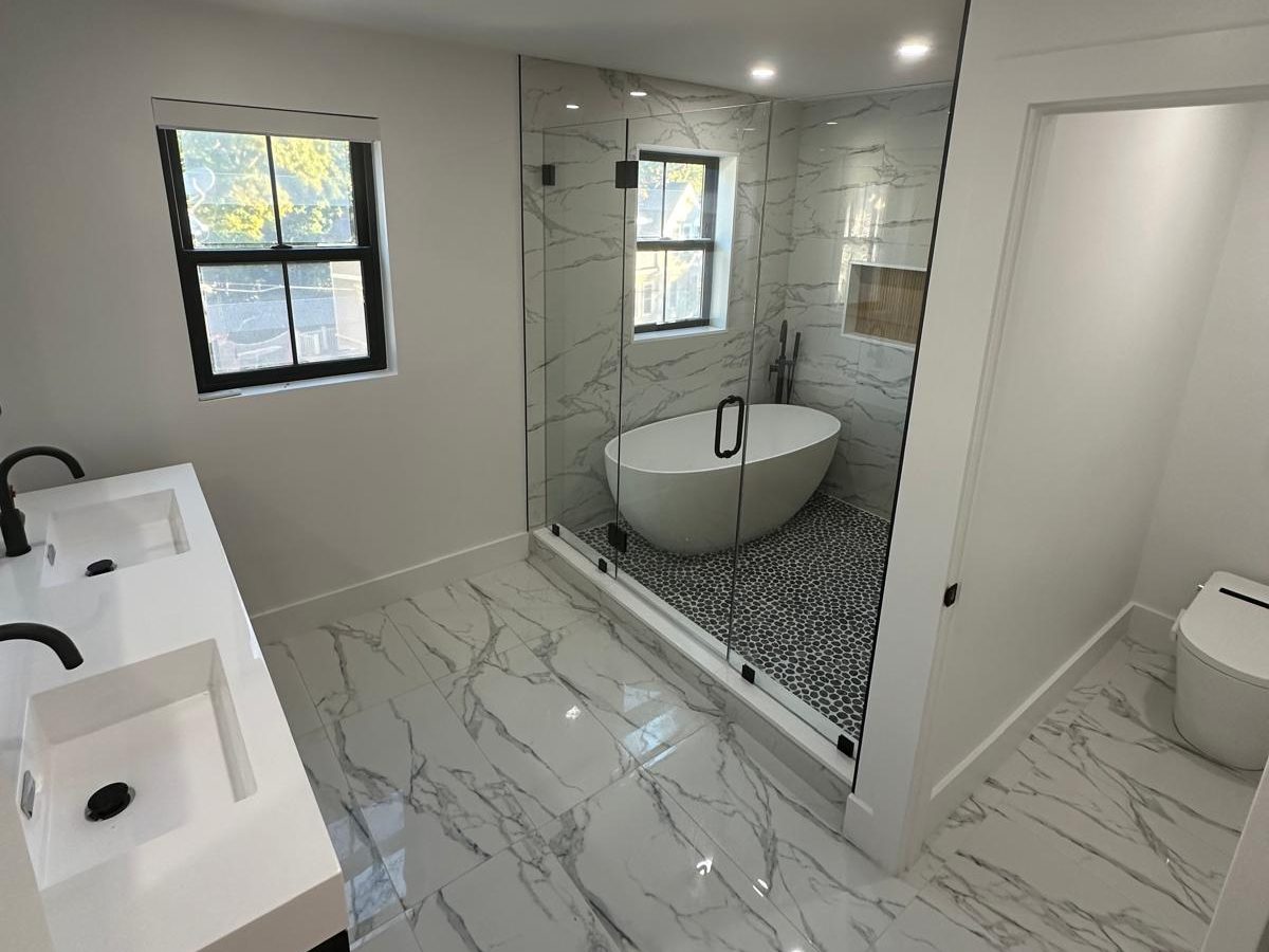 Primary bathroom with marble-look porcelain floor, floating double vanity and a glass-enclosed freestanding tub
