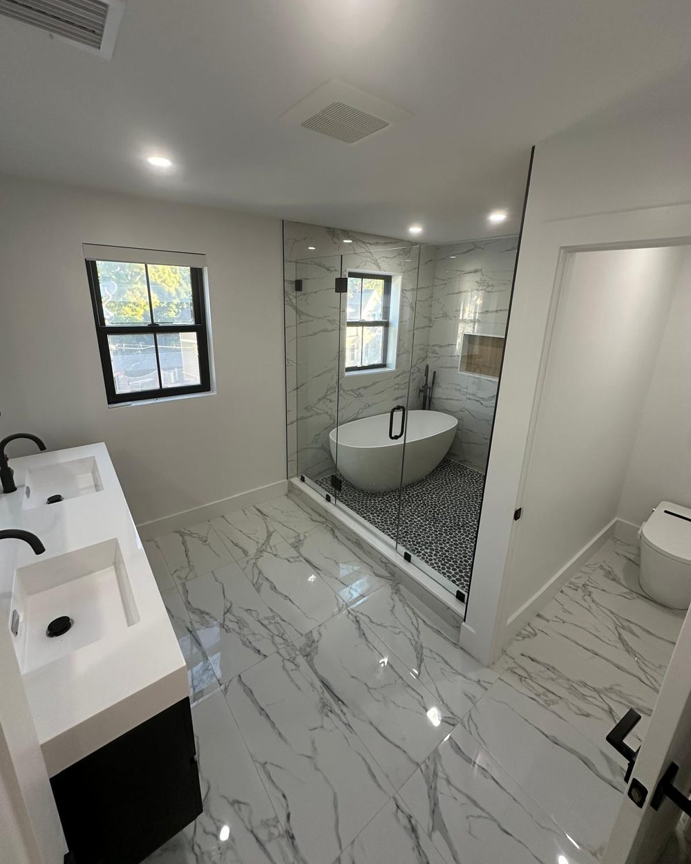 Primary bathroom with marble-look porcelain floor, floating double vanity and a glass-enclosed freestanding tub
