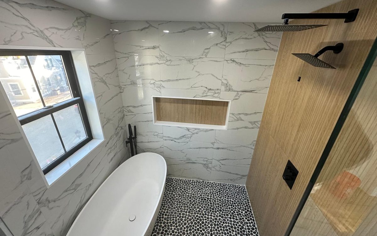 Wet room with a freestanding tub, black pebble mosaic floor, marble-look walls and a ribbed wood accent wall
