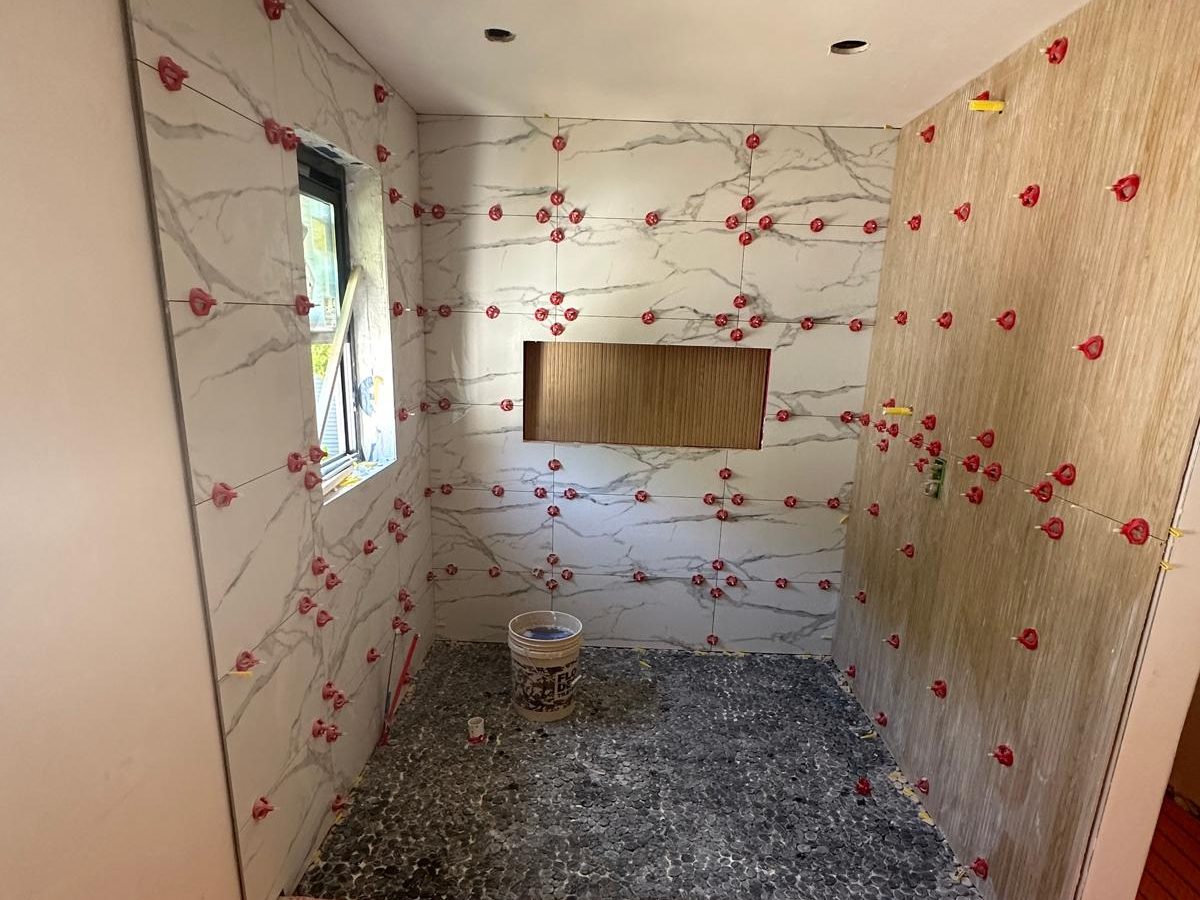 Shower walls in large-format marble-look porcelain held by leveling clips before grout