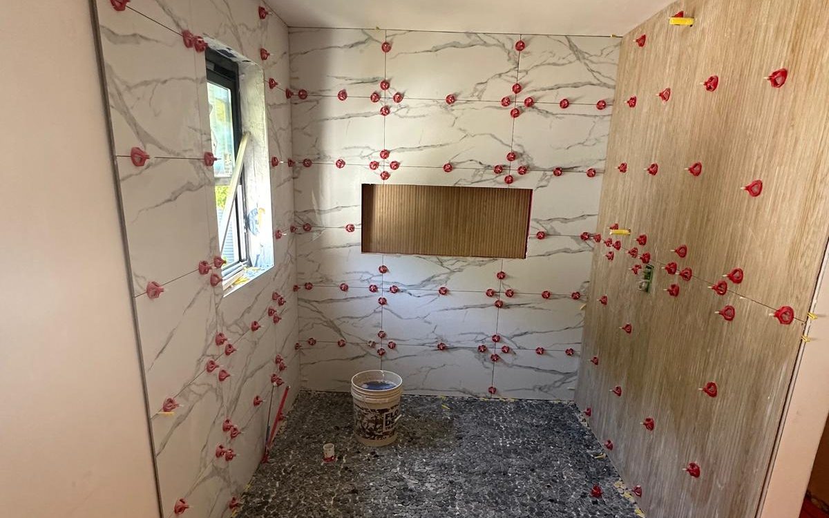 Shower walls in large-format marble-look porcelain held by leveling clips before grout
