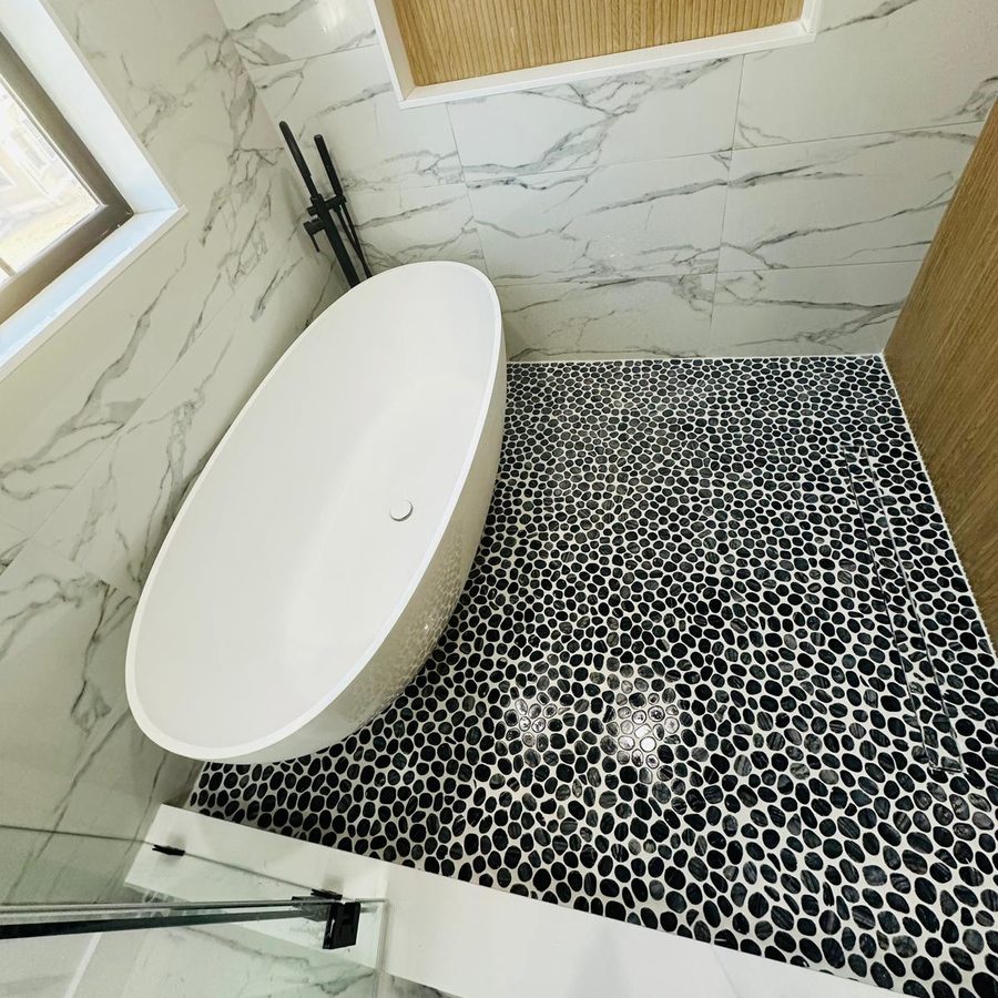 Freestanding tub on a black pebble mosaic floor with a matte black floor-mounted faucet
