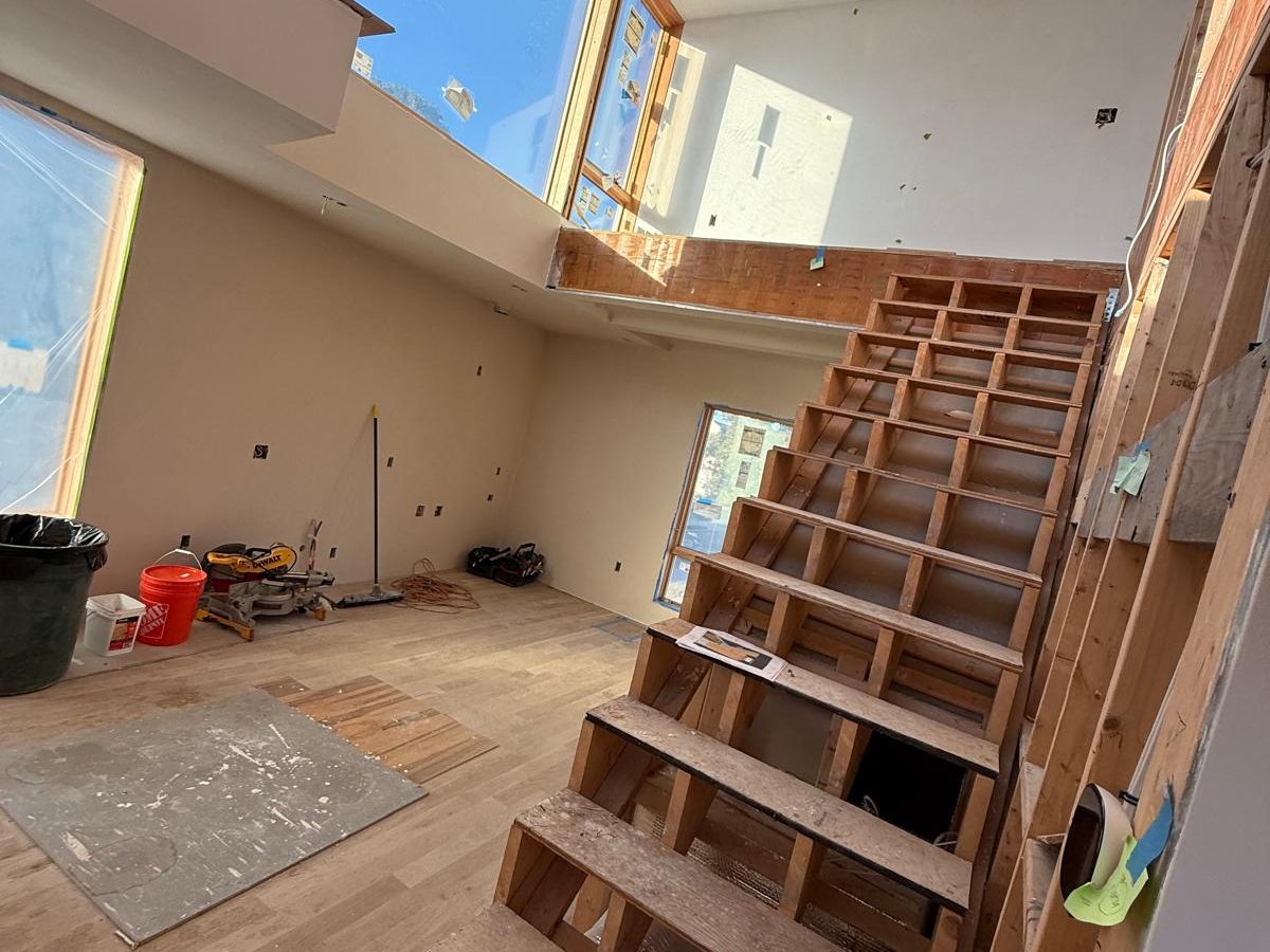 Open stair structure before finishing, in a double-height room with tall windows