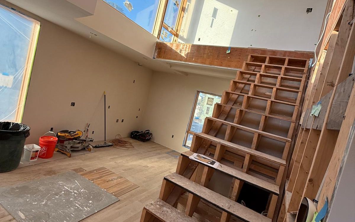 Open stair structure before finishing, in a double-height room with tall windows