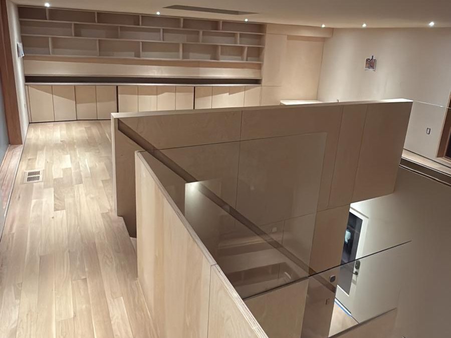 Upper-level library with built-in birch shelves, oak floor and a glass guardrail