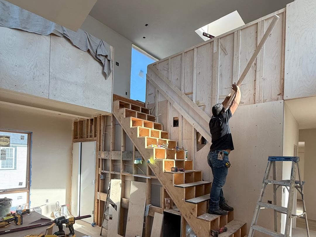 Carpenter fitting the stair wall framing while the stair is built on site