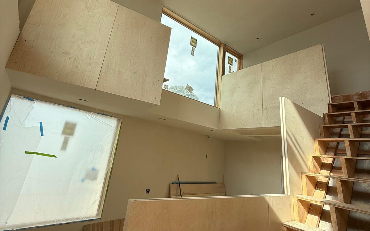 Birch plywood landing walls under tall windows in a double-height hall