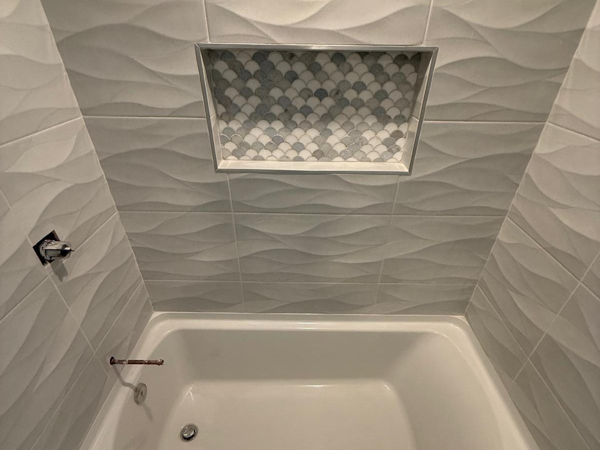 Tub surround in white wave-texture tile with a scalloped marble mosaic niche