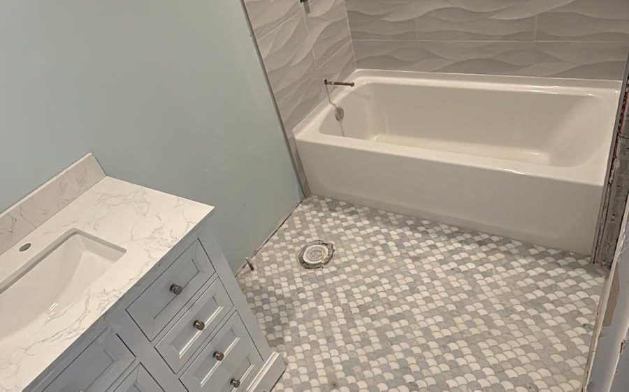Finished bathroom with wave-texture tub surround, scalloped marble mosaic floor and gray vanity