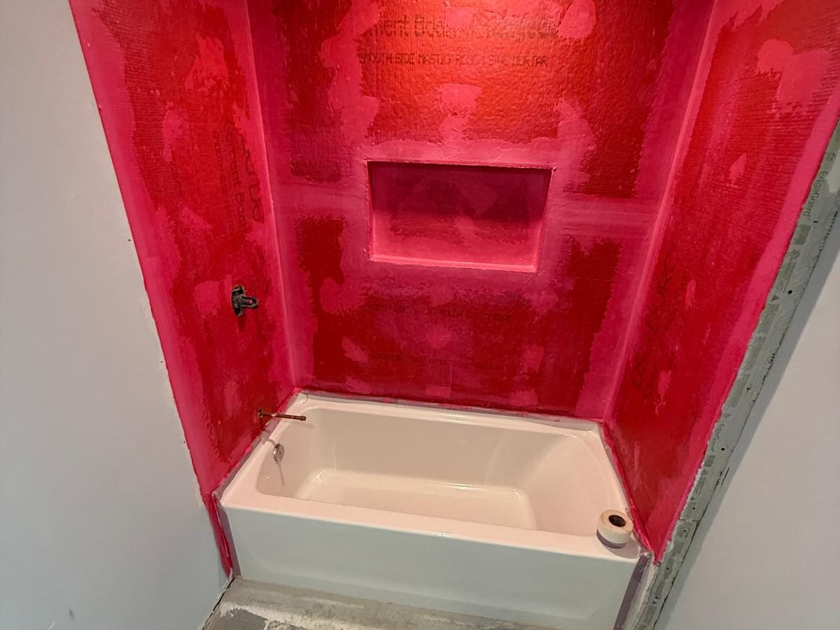 Tub surround coated in red waterproofing membrane, niche included, before tile