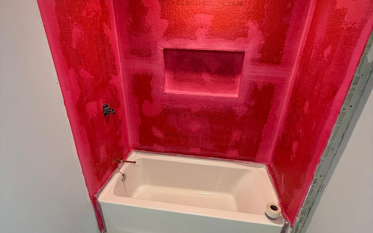 Tub surround coated in red waterproofing membrane, niche included, before tile