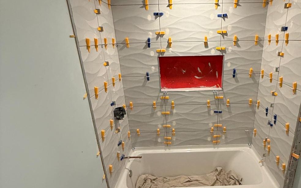 Large wave-texture tiles set with leveling clips around the tub, the niche still red