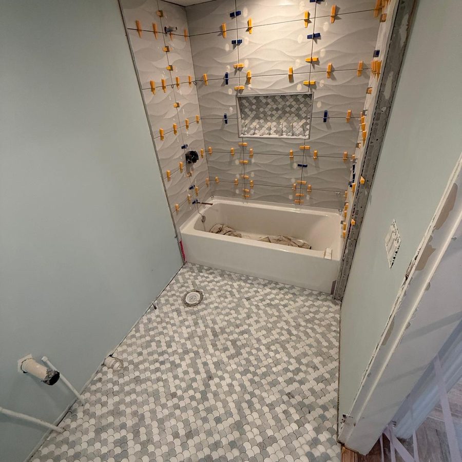 Scalloped marble mosaic floor installed while the wall tile is still held by leveling clips